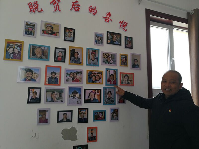 青海省黄南藏族自治州尖扎县尖扎滩乡来玉村扶贫第一书记李玉栋向记者介绍来玉村“脱贫后的喜悦”。照片墙集纳了村民们脱贫后的笑脸照片（2020年12月11日摄）。新华社记者 顾玲 摄